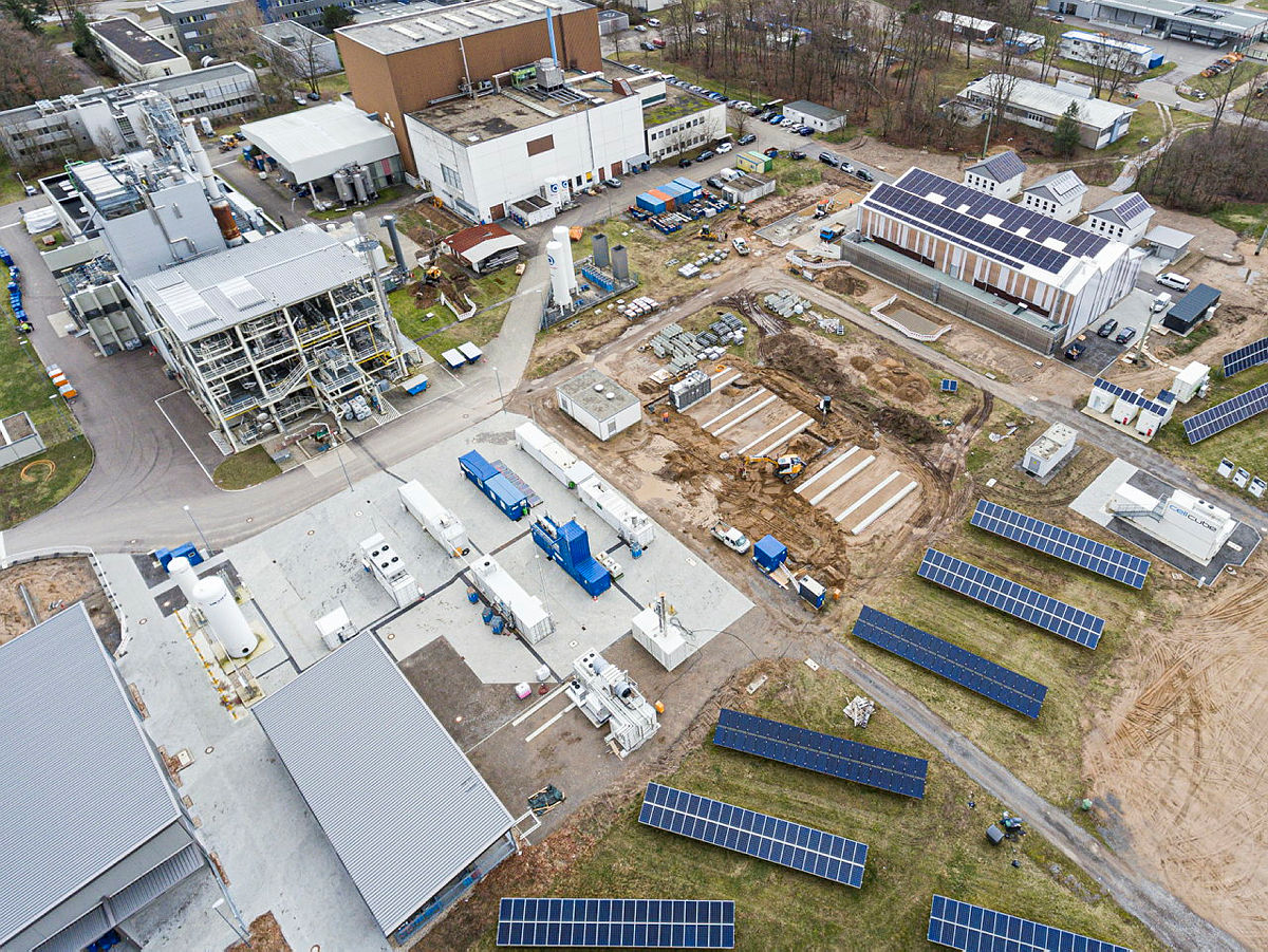 Luftaufnahme einer Industrieanlage mit Solarpaneelen und Gebäuden.