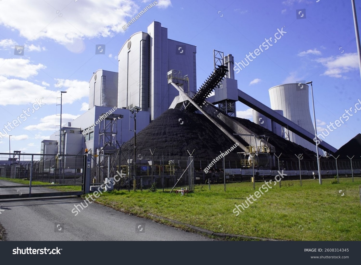 Kohlekraftwerk mit Kohlehaufen und Förderband unter blauem Himmel.